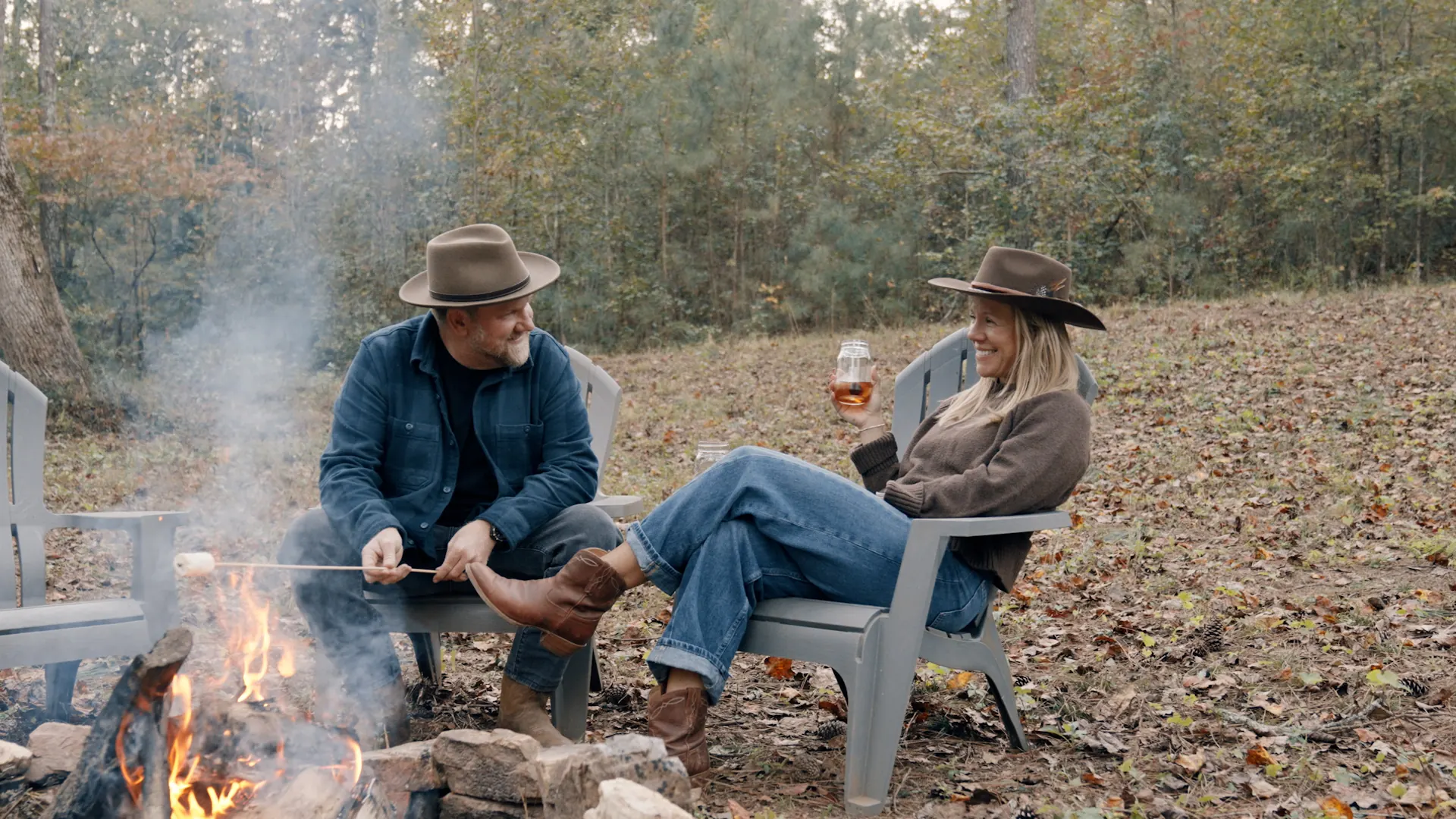 A couple relaxing by a fire pit at the edge of a wooded clearing
